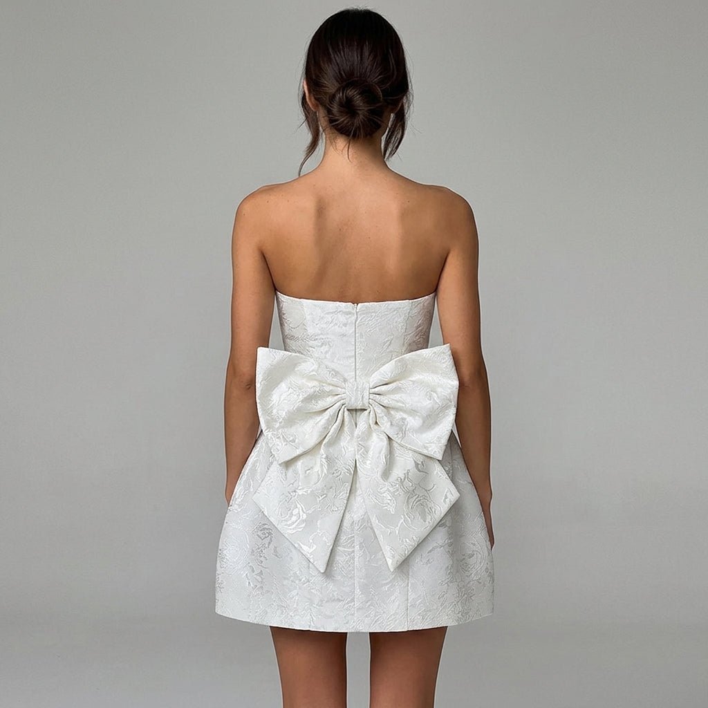 Back view of white strapless mini dress featuring a dramatic oversized bow detail and invisible zipper