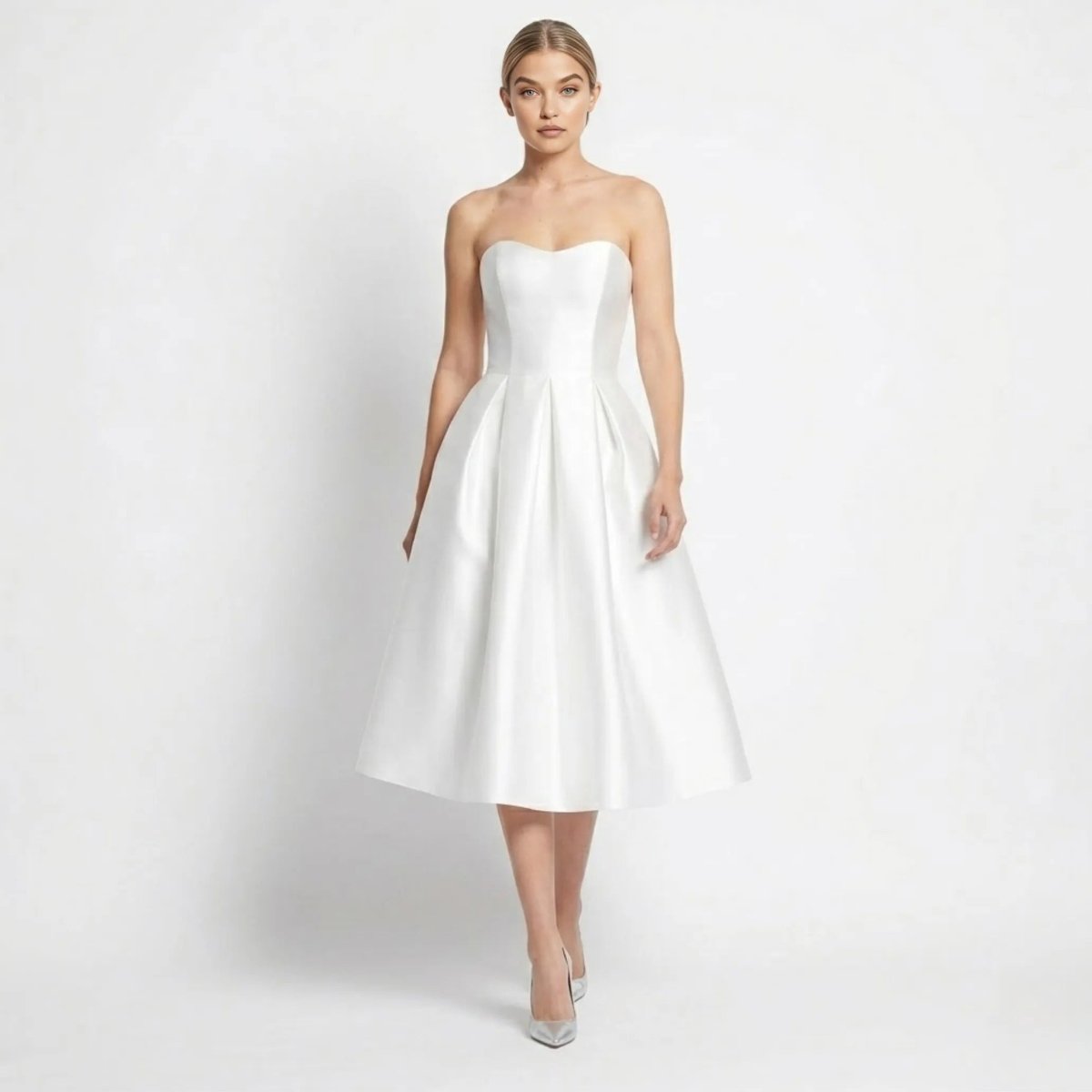 Woman walking wearing a white strapless satin midi dress with pleated A-line skirt by Kouvr.