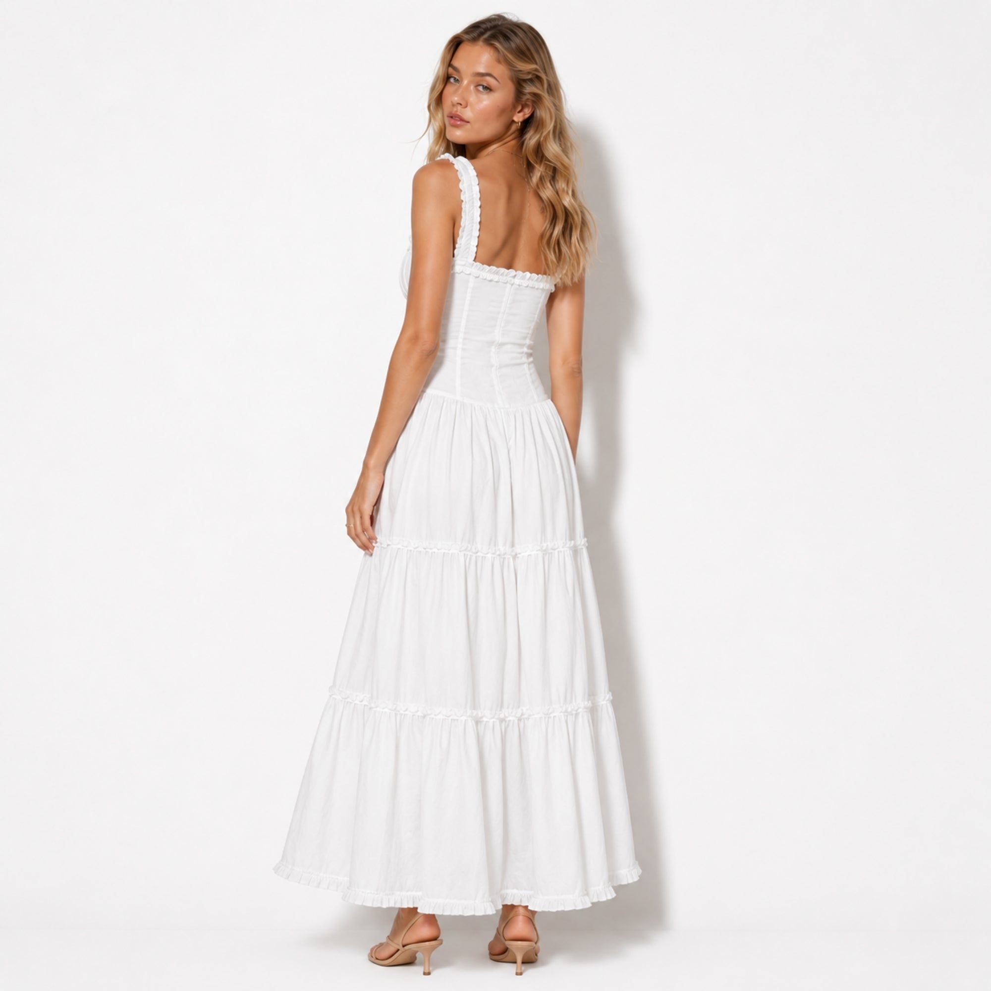 Woman looking over shoulder wearing a white tiered ruffle maxi dress showing the tailored corset back and wide ruffle straps.
