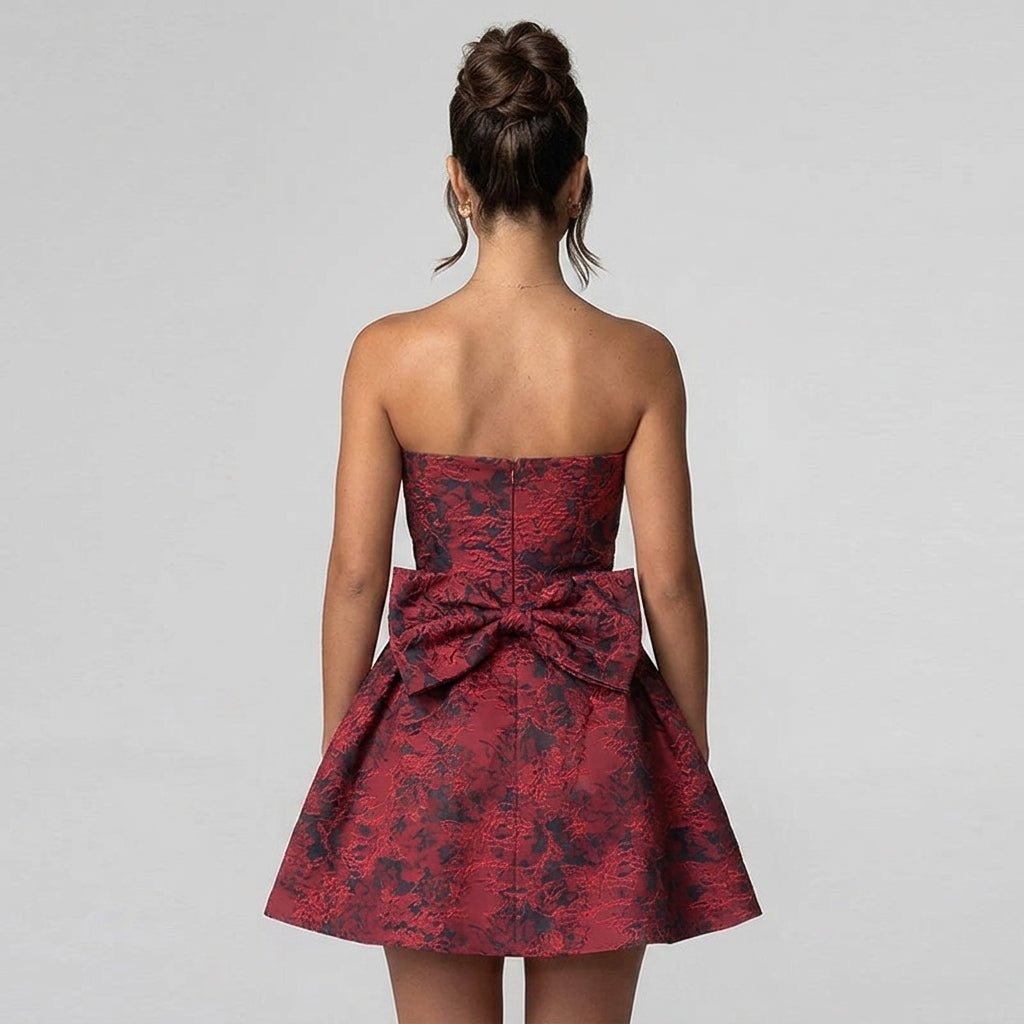 Back view of a wine red floral jacquard mini dress showcasing a dramatic oversized statement back bow and concealed zipper closure.