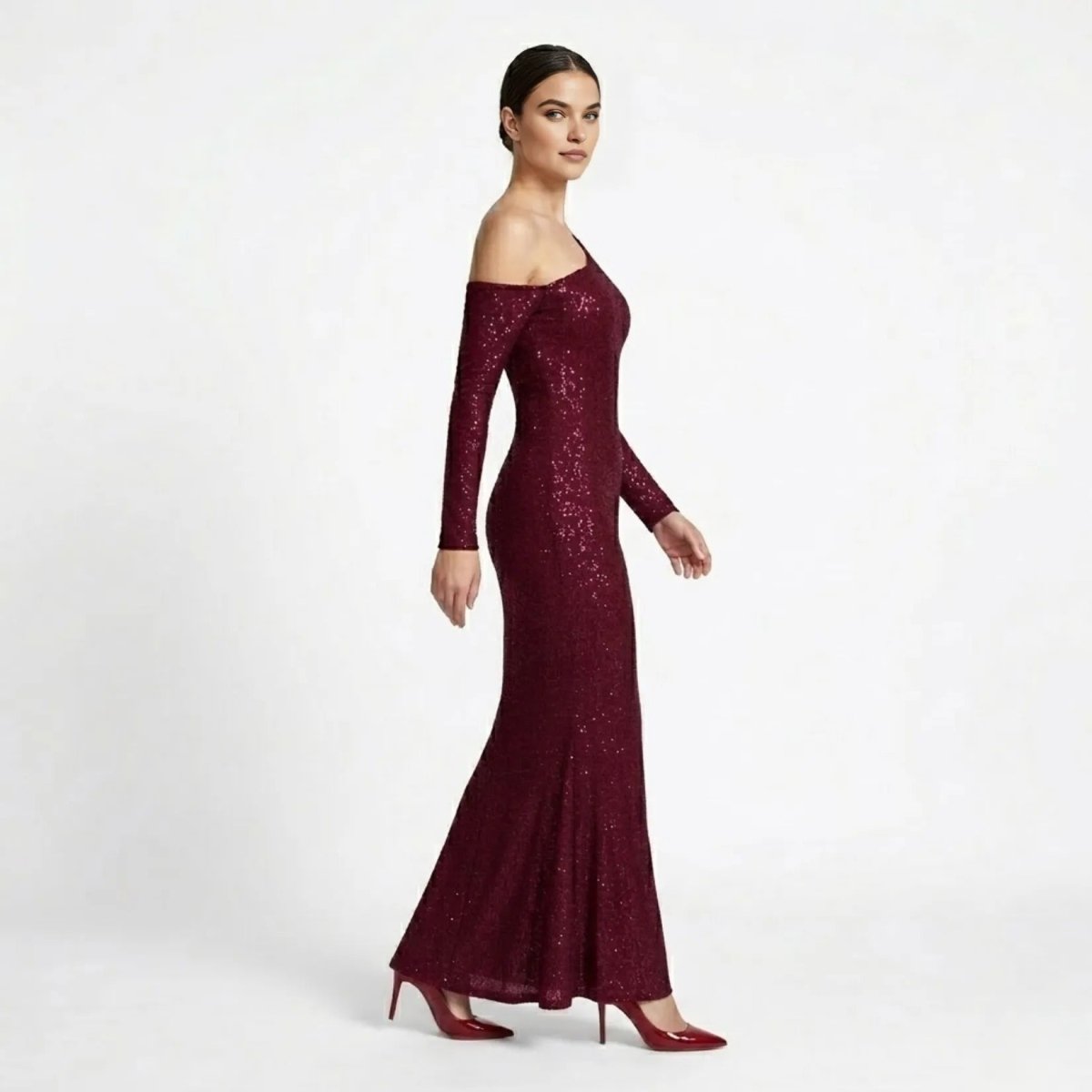 Side profile of a woman modeling an elegant wine red sparkly evening gown with asymmetric neckline. 