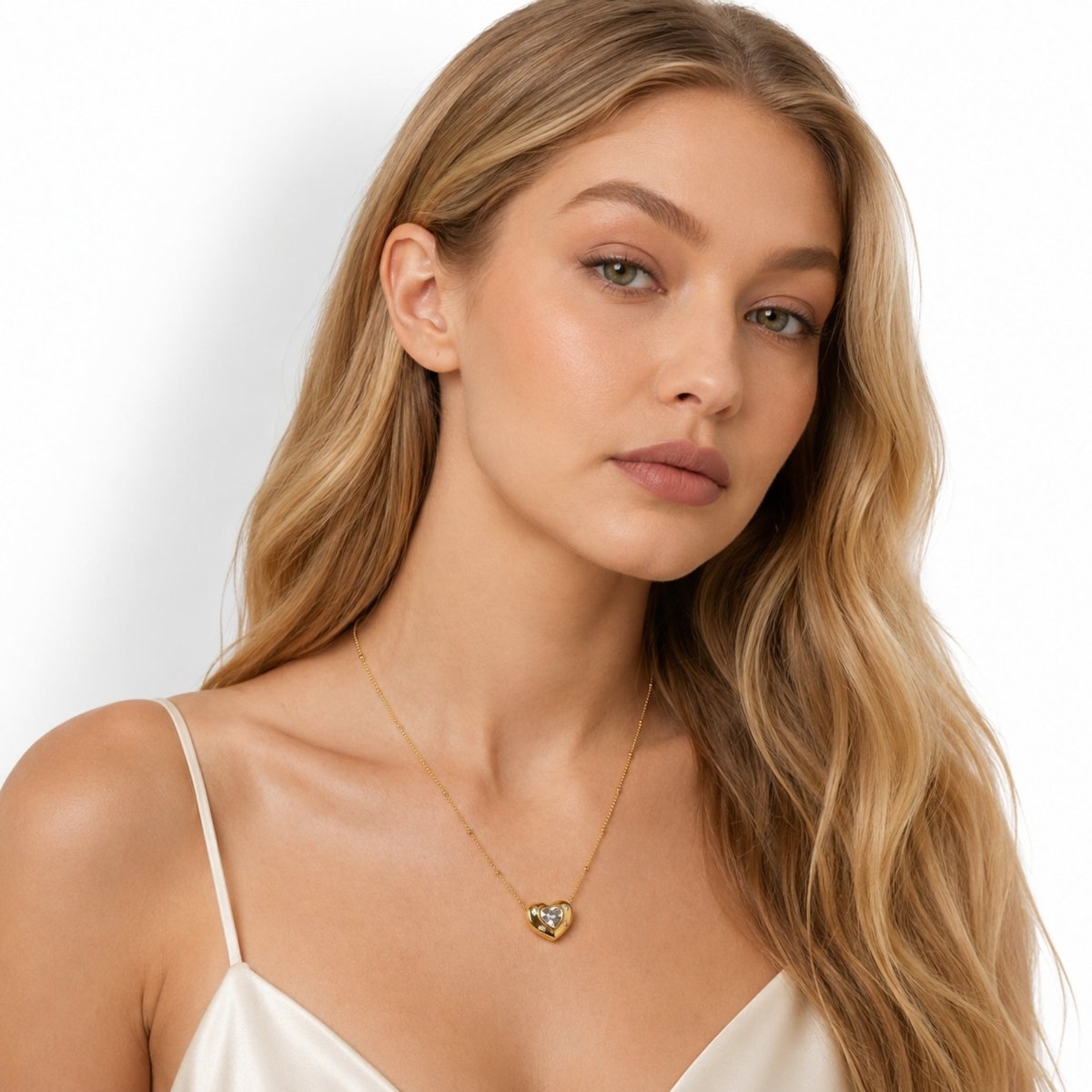 Beautiful blonde model wearing the Kouvr gold heart pendant necklace with a white silk top, showcasing everyday luxury styling.