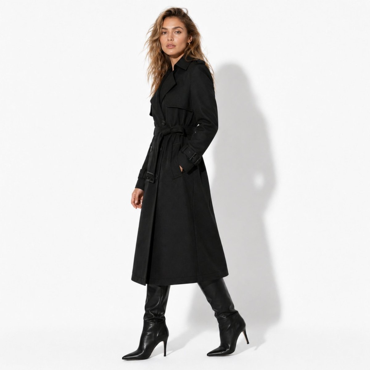 Side view of woman wearing a black belted longline trench coat with pockets