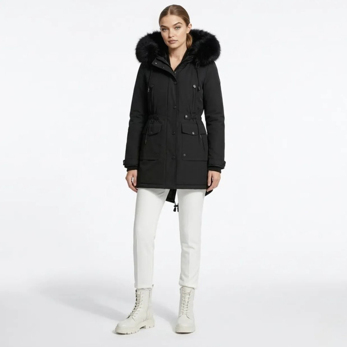 Woman wearing a black mid-length winter parka coat with faux fur hood, styled with white pants and boots, standing against a white background.
Image 2 Name: womens-black-faux-fur-hooded-parka-side.jpg
