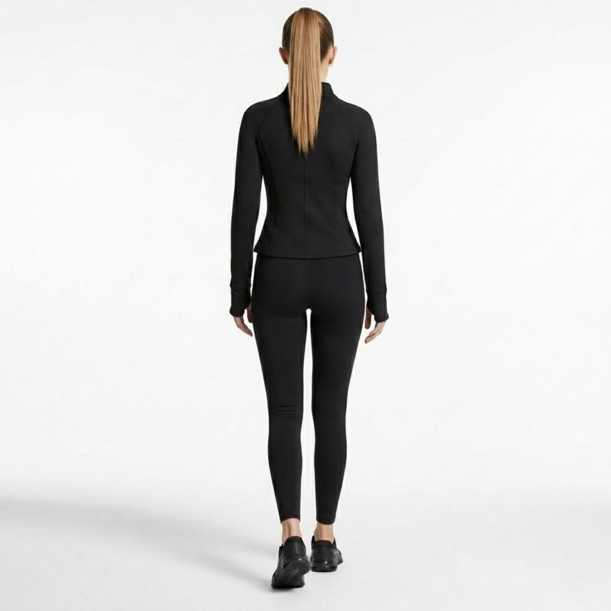 Full length back view of woman walking in complete black athletic set featuring Kouvr structured zip jacket.