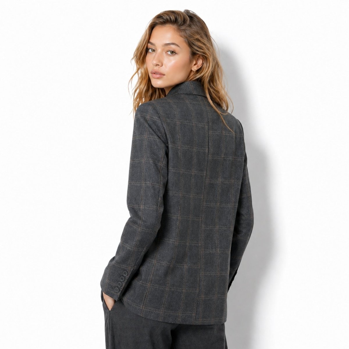  Back view of female model wearing the Kouvr tailored grey check jacket showing back seam and cuff button details.