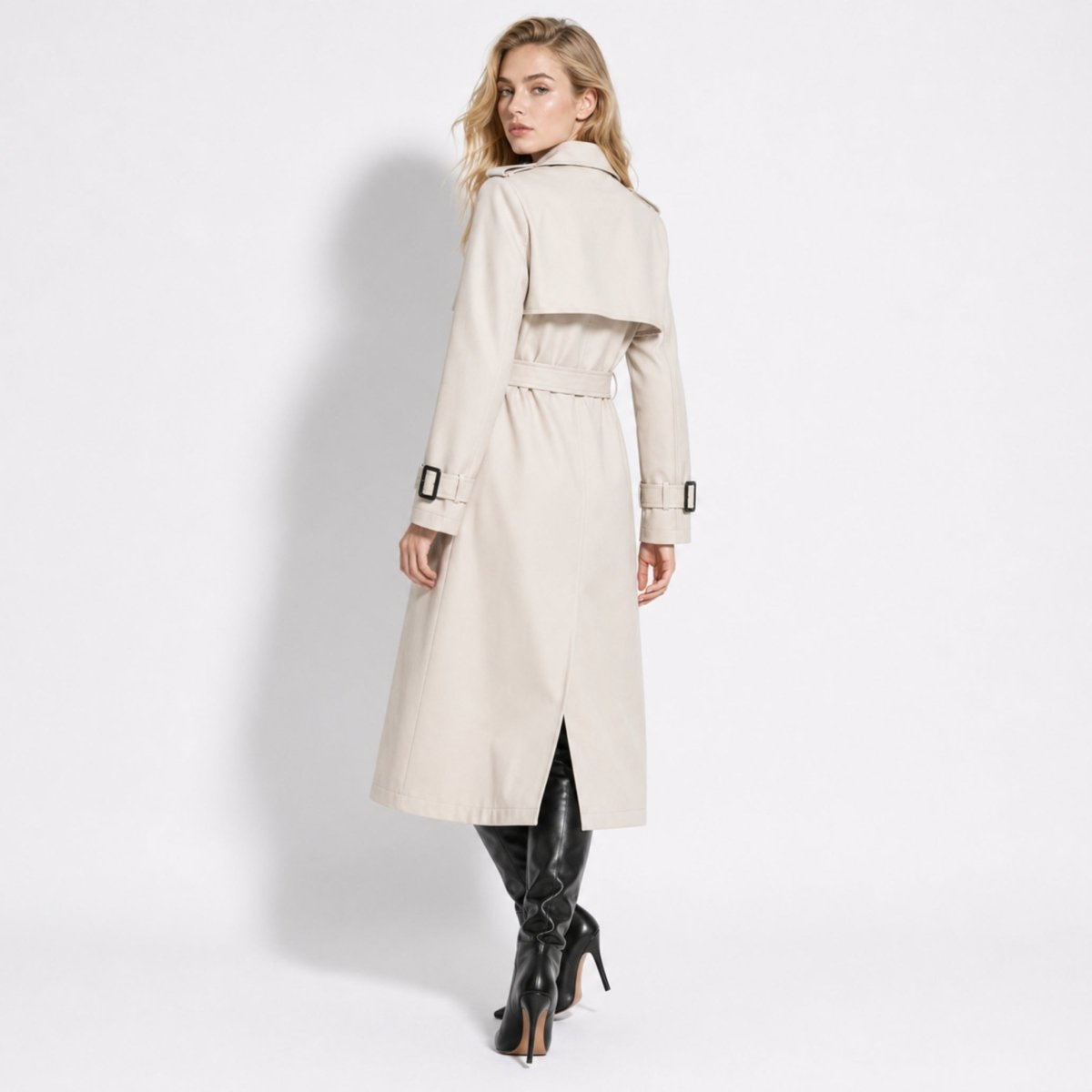Back view of a women's beige trench coat highlighting the traditional rear storm flap, tied waist belt, and center back vent slit.
